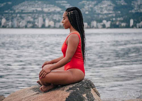 Free Woman in Red Swimsuit Sitting on a Big rock while Meditating Stock Photo
