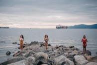 2 Women in Bikini Sitting on Rock Near Sea