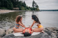 2 Women in Bikini Lying on Rock Near Body of Water