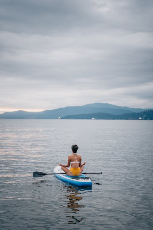 Free Woman Sitting on a Paddle Board Meditating Stock Photo