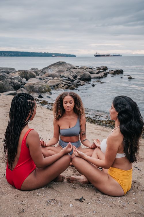 Free Three women meditating on a serene beach, promoting tranquility and diversity. Stock Photo