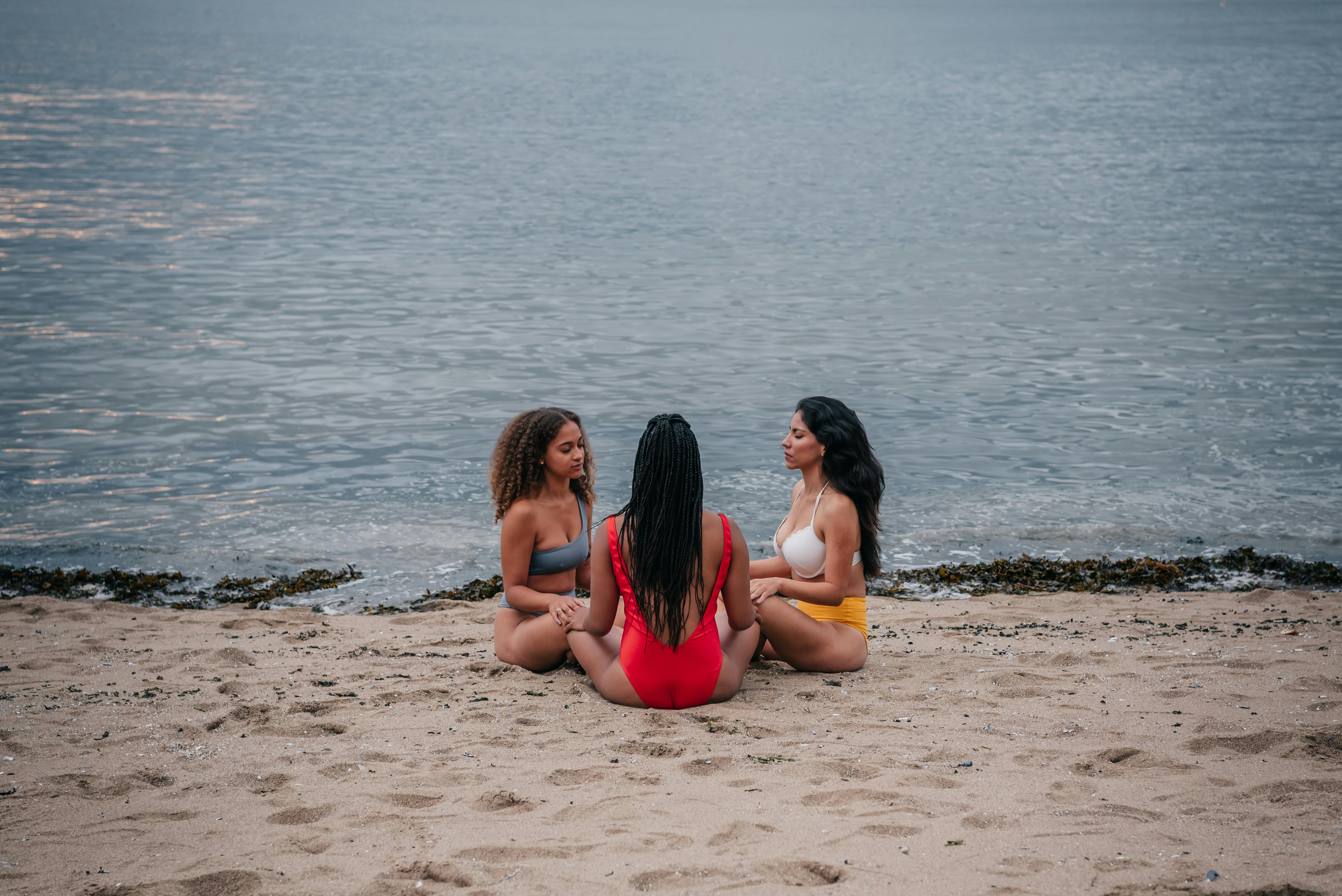 Three women meditating together on a serene seaside beach, embracing mindfulness and unity.