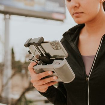 Close-up of a woman holding a drone controller with smartphone outdoors.