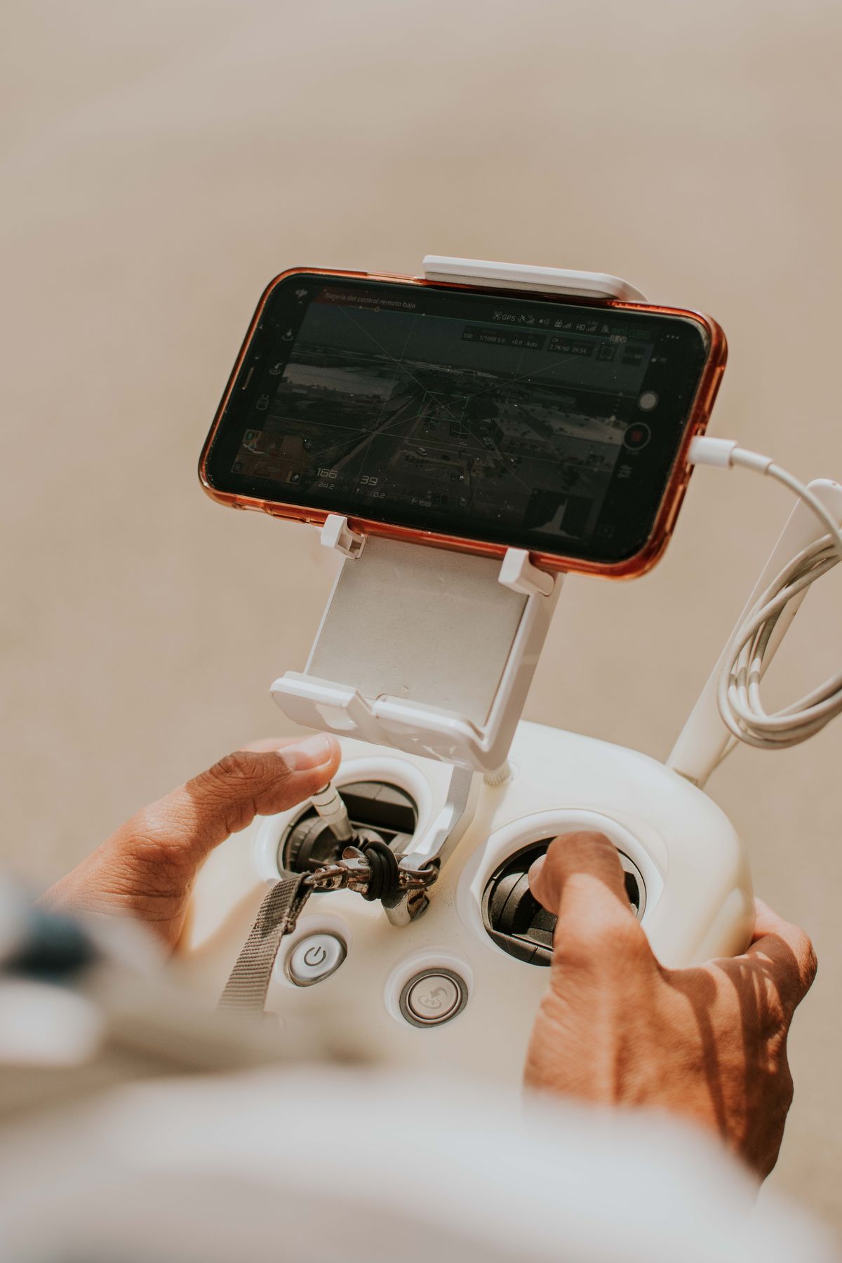 Instructor hands guiding a student on a drone controller with phone display
