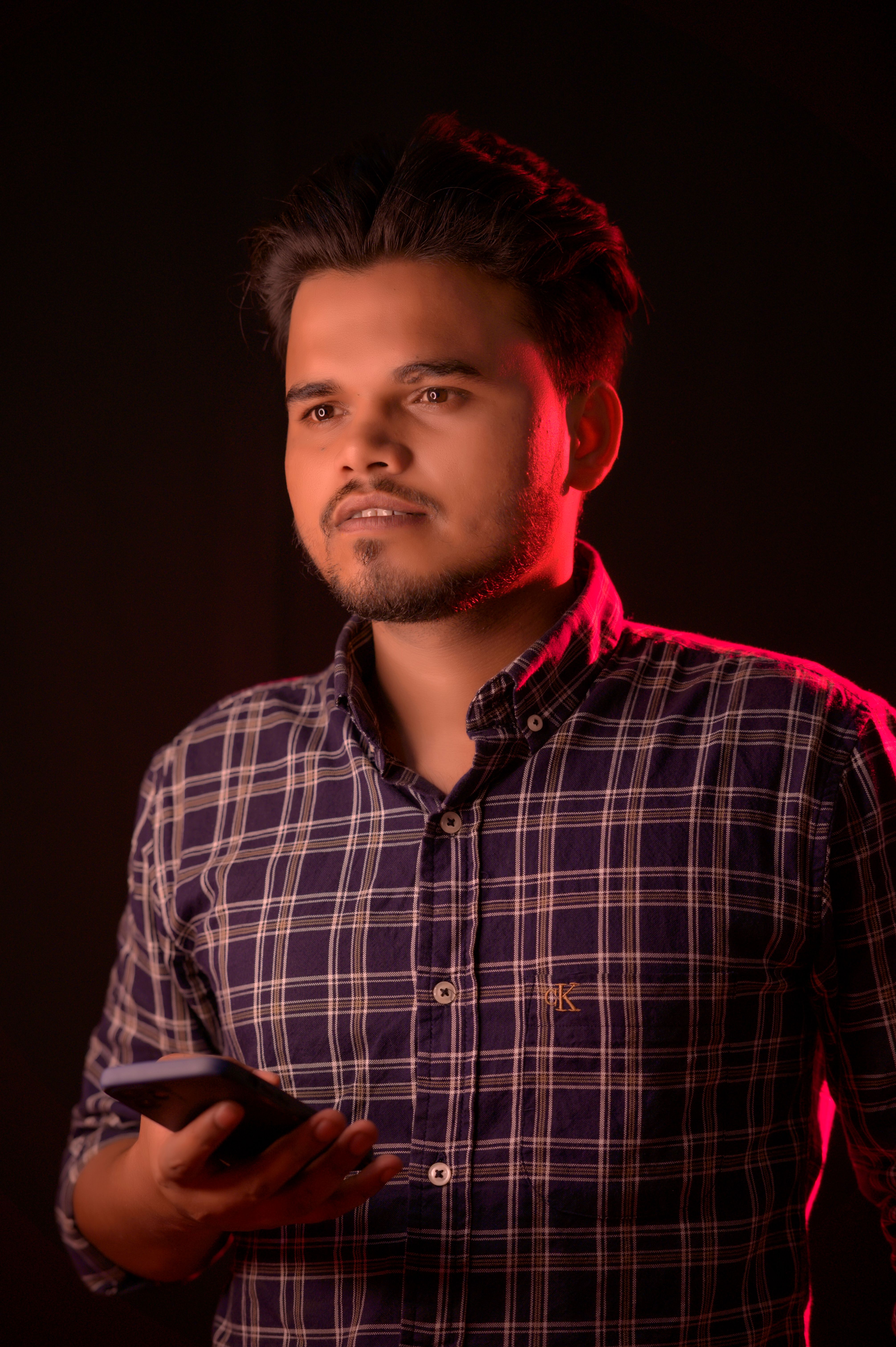 Man in plaid shirt holding a smartphone, lit in a studio setting with red highlights.