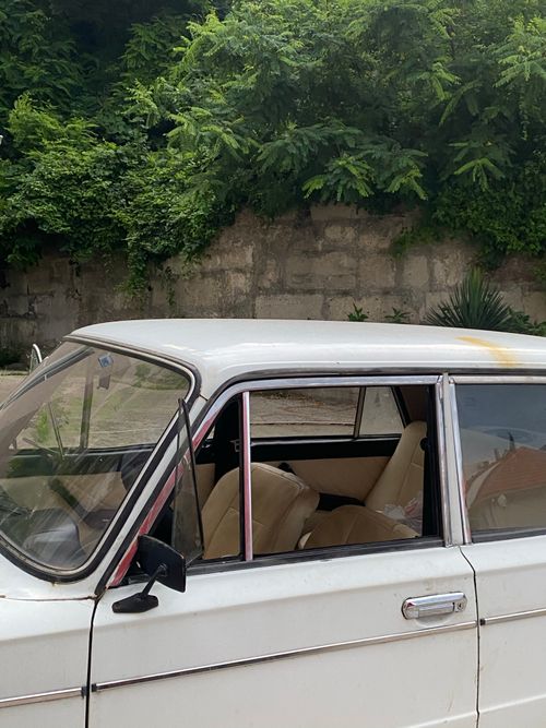 Free A classic white car parked beside a stone wall with lush greenery above. Stock Photo