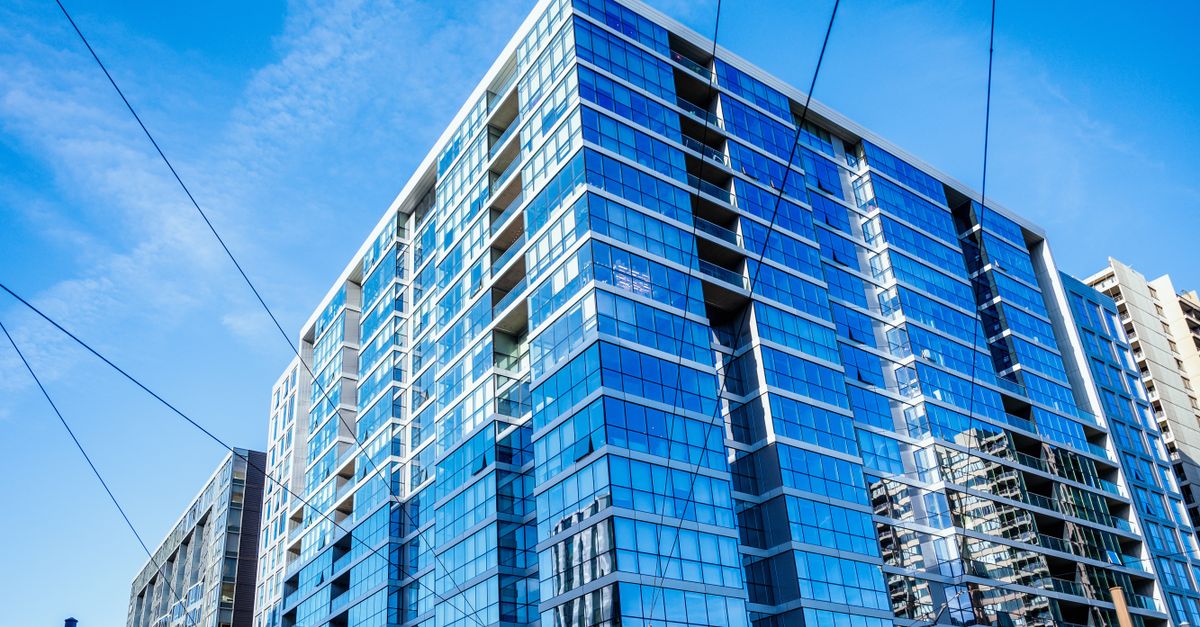 Low-angle view of a modern glass-clad building reflecting blue sky and clouds.