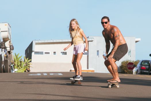 A man and young girl skateboarding on a sunny urban street, showcasing a fun outdoor activity.