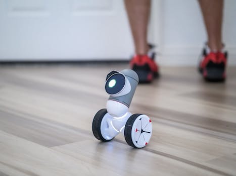 A close-up of a modern wheeled robot on a wooden floor with legs in the background.