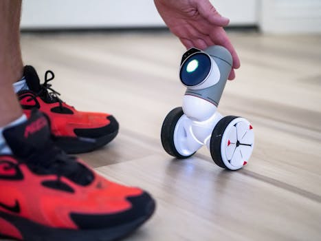 Close-up of a small toy robot being held near a person's foot in bright sneakers, showcasing innovation.