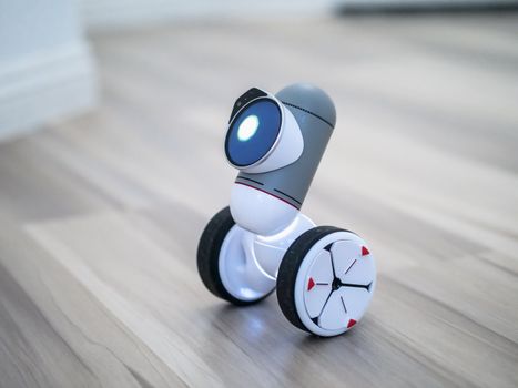 Close-up of a modern toy robot with wheels on a wooden floor, emphasizing its design and technology.