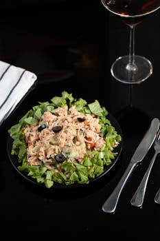 Close-up of a vibrant tuna salad with olives and lettuce on a black plate.