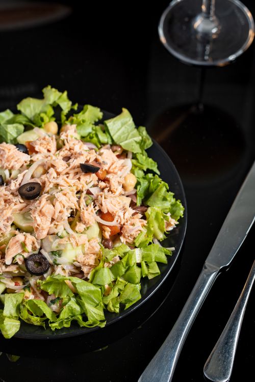 Free A vibrant tuna salad with fresh vegetables, olives, and lettuce on a black plate. Stock Photo