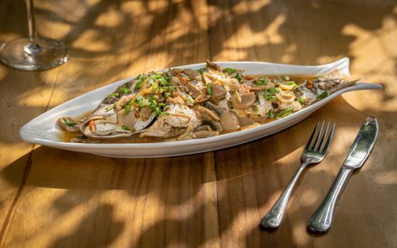A tempting dish of steamed fish garnished with mushrooms and green onions, beautifully plated on a wooden table.