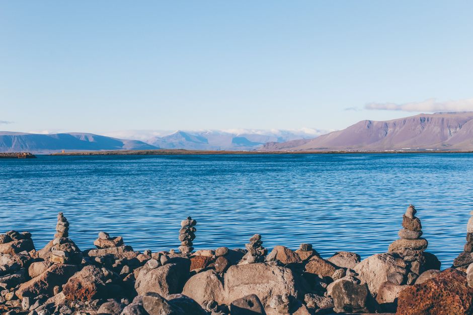 Serene seascape of stacked rocks along Reykjavik's coast with distant mountains under a clear sky.