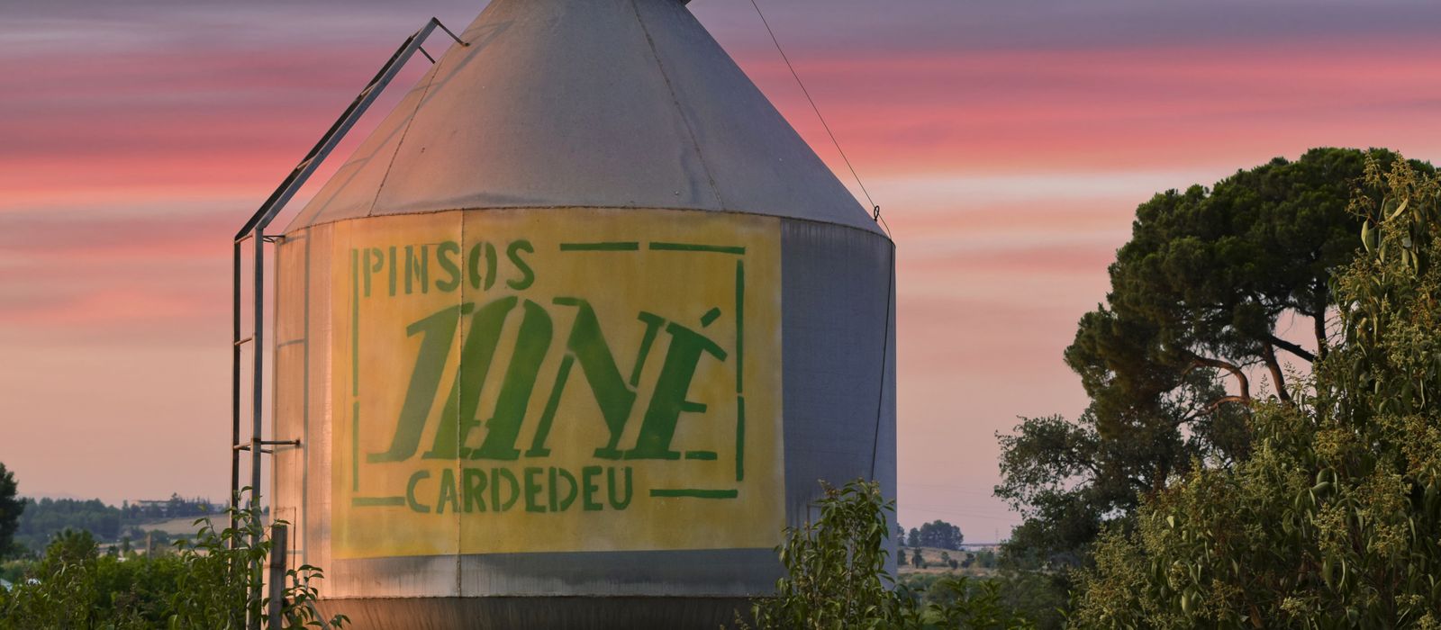 Industrial silo amidst lush greenery in Sant Cugat del Vallès, Spain, at sunset.