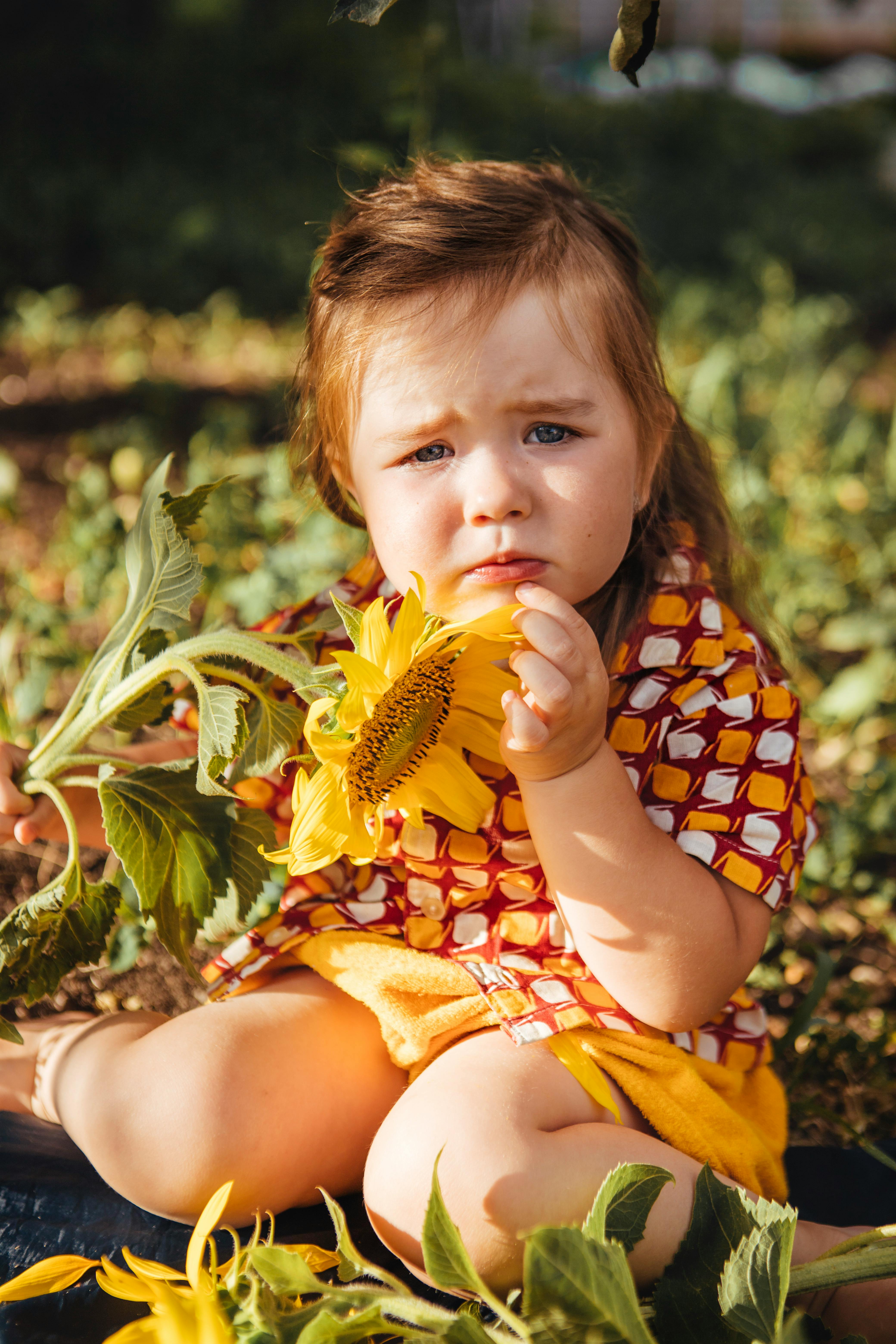 Adorable young girl holding a sunflower while sitting outside. Perfect for family or summer-themed projects.