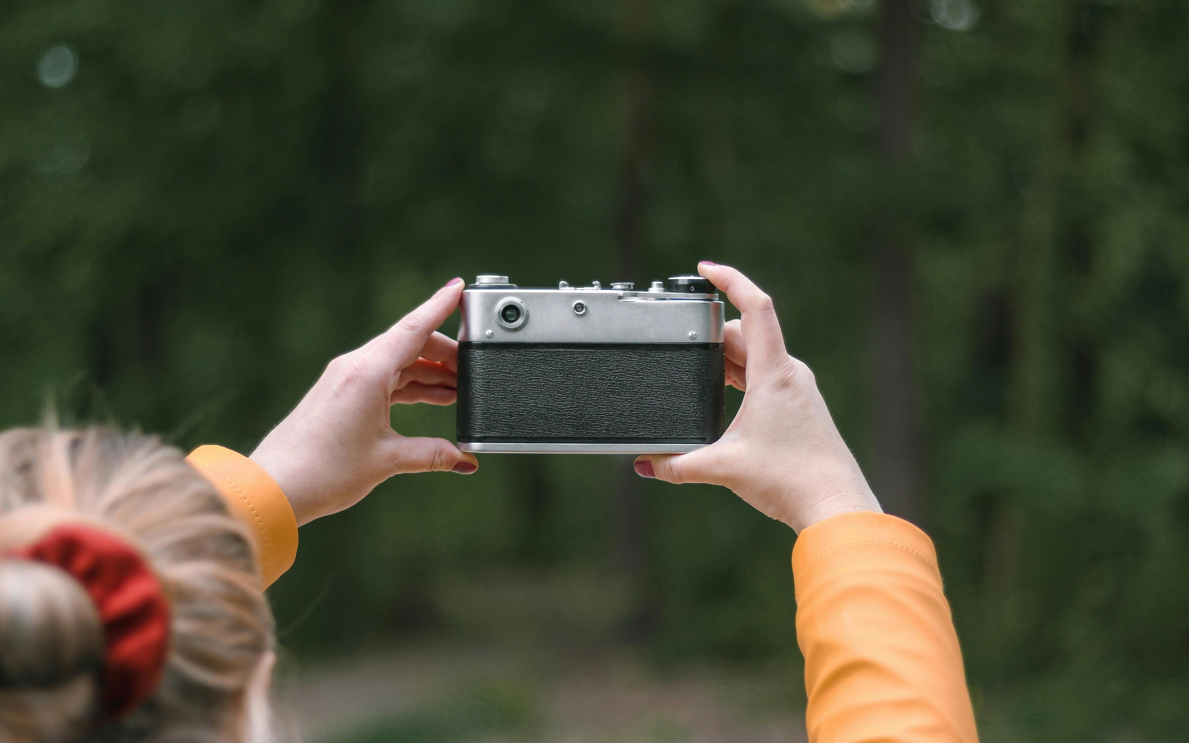 A person holding a vintage camera outdoors in a forest setting, capturing the essence of nature photography.