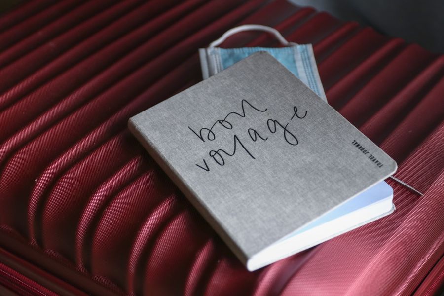 Close-up of a travel journal and mask on a red suitcase, symbolizing preparation for a voyage.