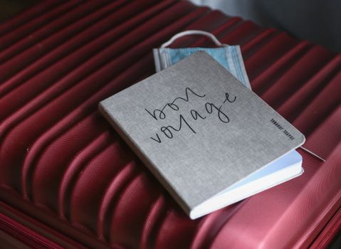 A Gray Notebook and Face mask on  Red Suitcase 