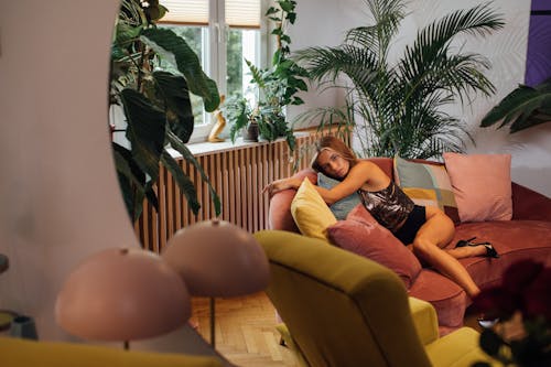 A Woman in Sexy Outfit Sitting on a Couch Near Potted Plants