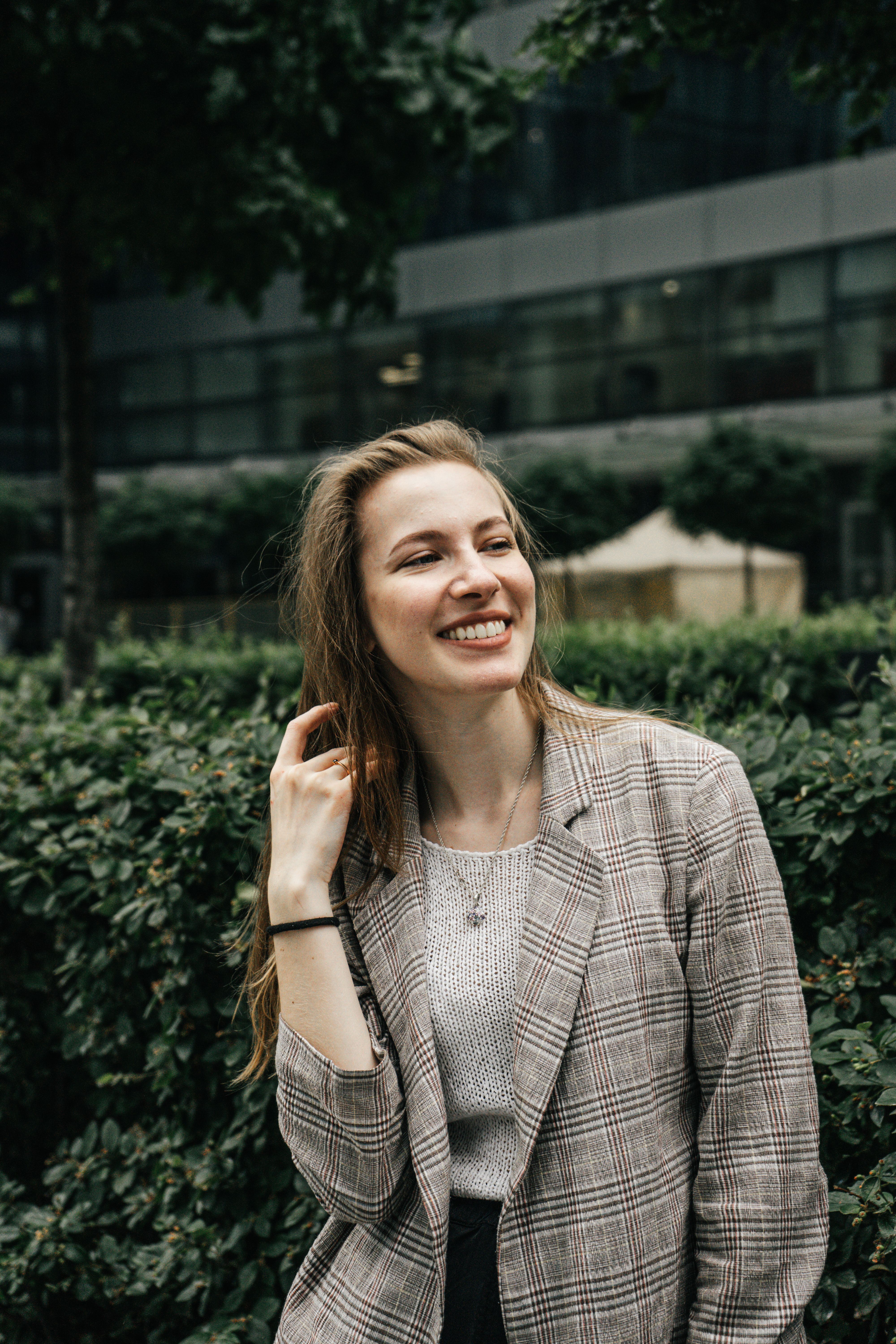 A young woman in a plaid jacket smiling confidently outdoors.
