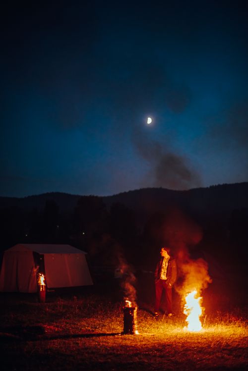 Free A camper enjoys a bonfire under the starry night sky, capturing the essence of outdoor adventure. Stock Photo