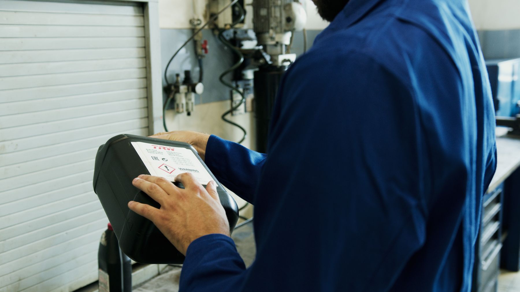 Mechanic using a handheld diagnostic tool beside a vehicle in an automotive workshop.
