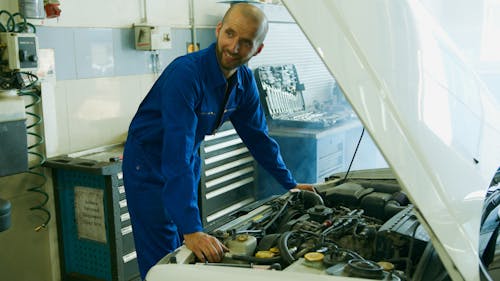 Free Man in Blue Overall Standing Beside White Car's Hood Stock Photo