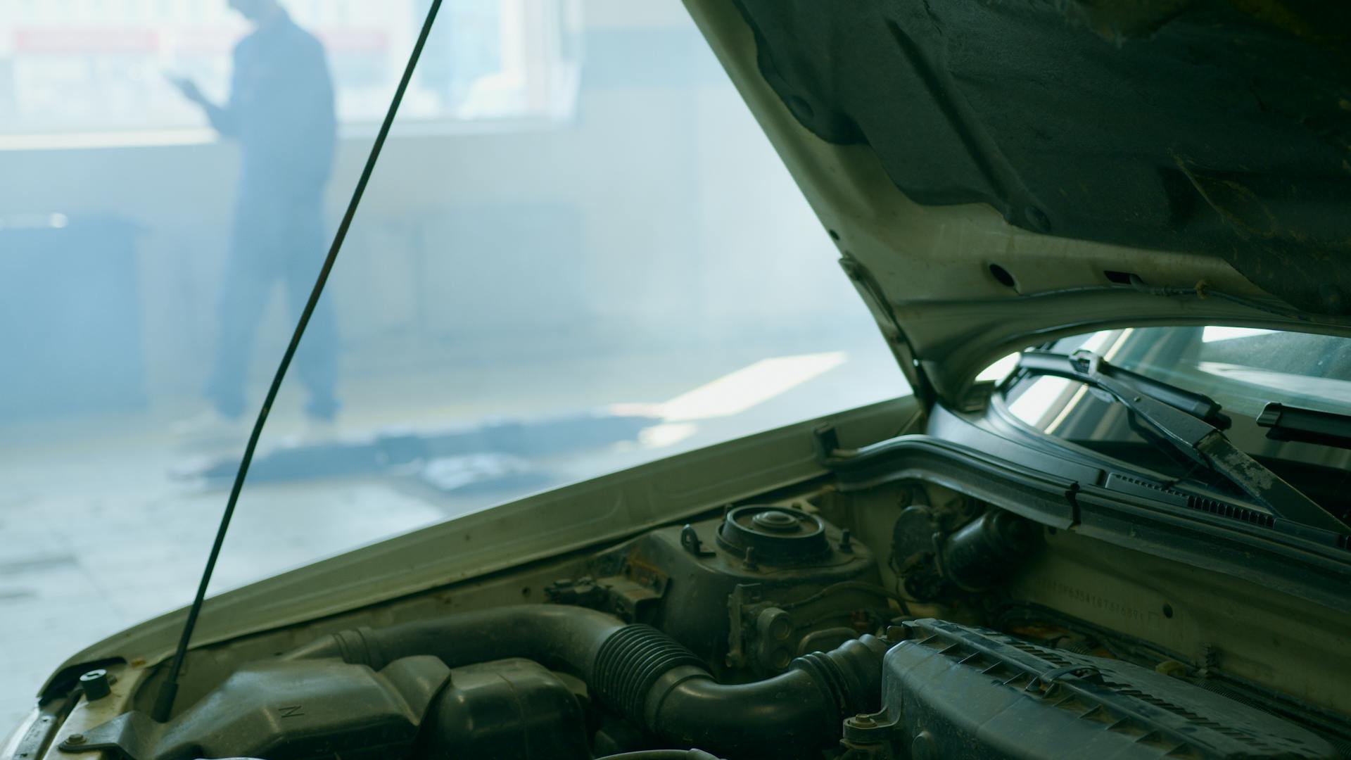 Detailed view of an open car hood in a mechanic workshop with a mechanic blurred in the background.