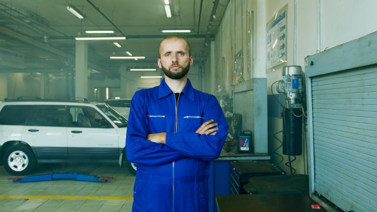 A Man In Blue Boilersuit Standing Near A White Car