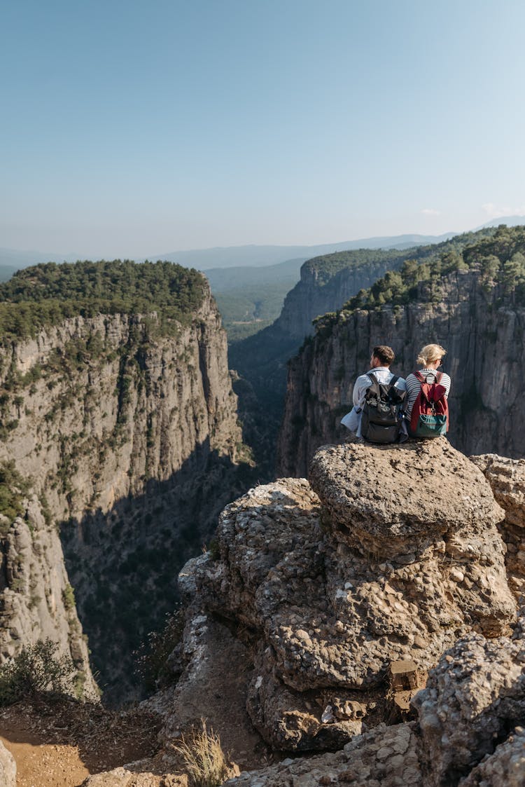 Back View Of A Romantic Couple Sitting On The Rock In Front Of Mountains 