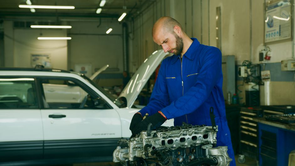 Stock photo: Mechanic in a blue coverall inspecting car engine in a garage workshop