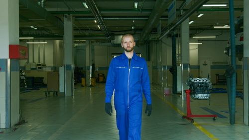 Free A mechanic wearing a blue jumpsuit walks confidently through a modern auto workshop. Stock Photo