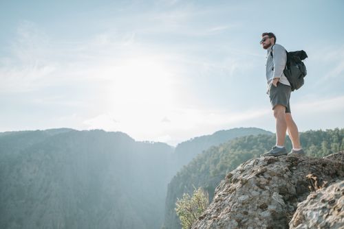 Free Man standing on a rocky mountain peak, gazing at scenic views under clear skies. Stock Photo