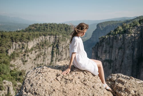 Free Woman in White Dress Sitting on Rock Formation Stock Photo