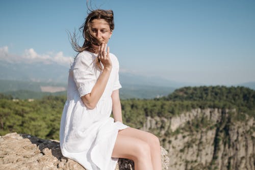 Free A Woman in White Dress Sitting on Brown Rock Stock Photo