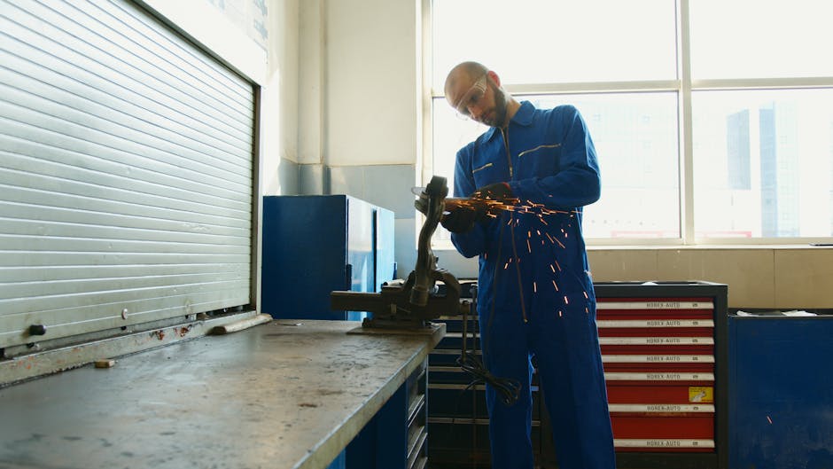 A technician in overalls uses a grinder tool, creating sparks in a workshop setting.