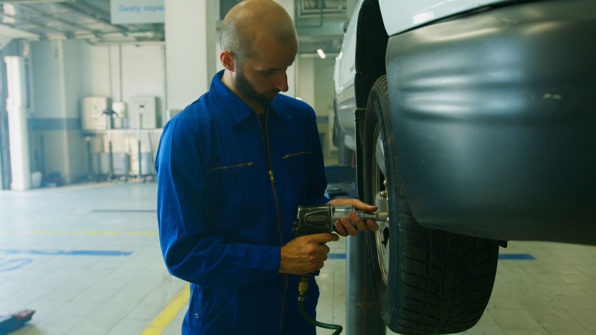 Mechanic using a pneumatic impact wrench to remove lug nuts from a car wheel in a home garage