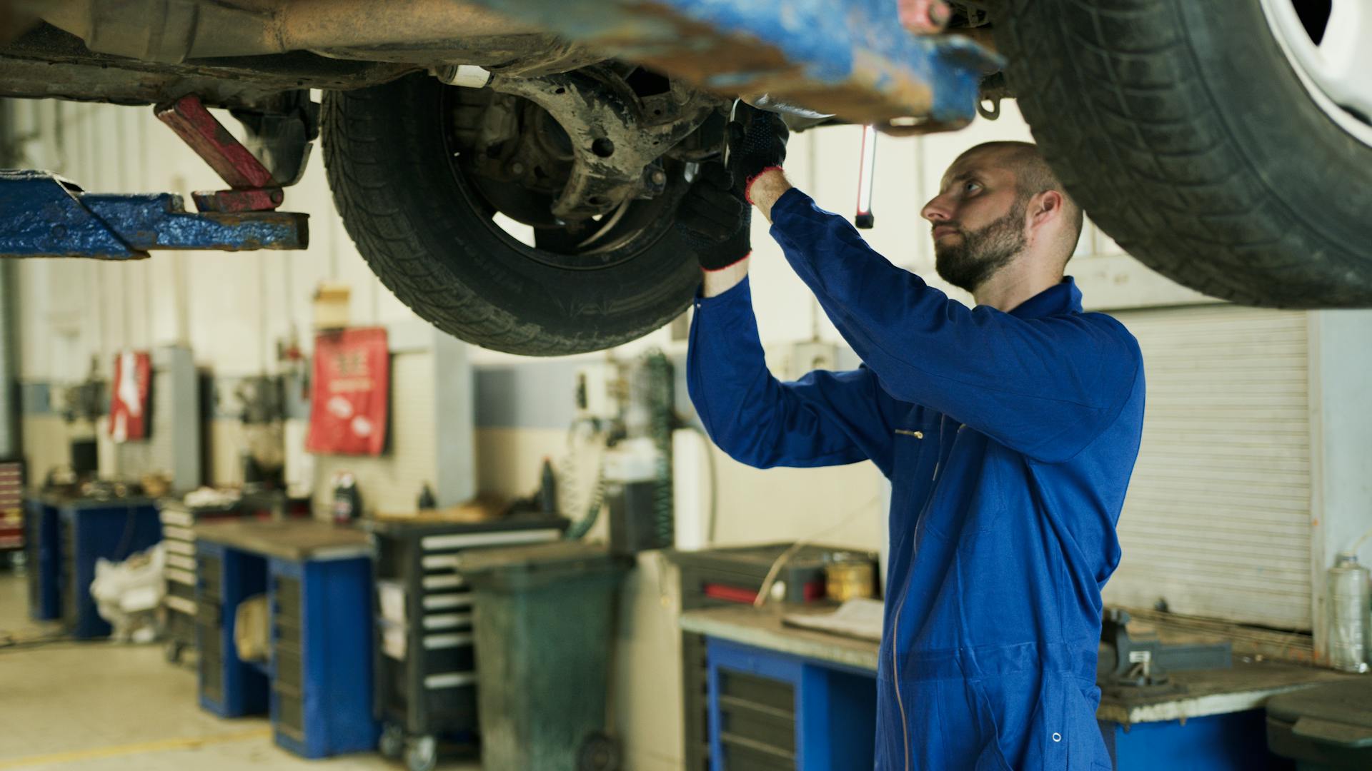 Man in Blue Work Clothes Fixing a Car