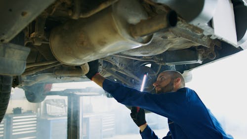 Man in Blue Coverall Checking Under A Vehicle