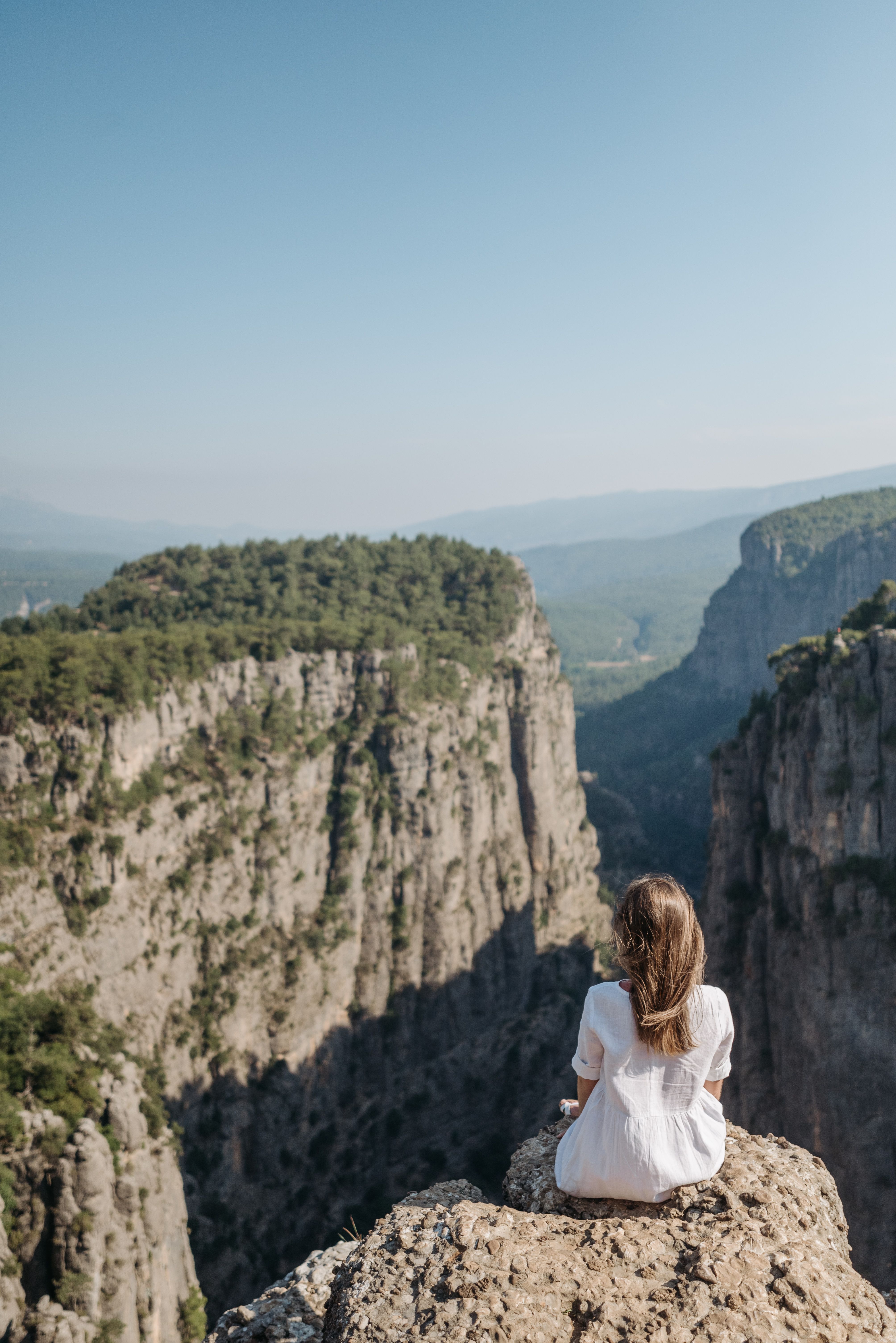 Back View of a Woman in White Dress Sitting on a Rock Looking at the ...