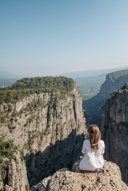 Free Back View of a Woman in White Dress Sitting on a Rock Looking at the Canyon Stock Photo