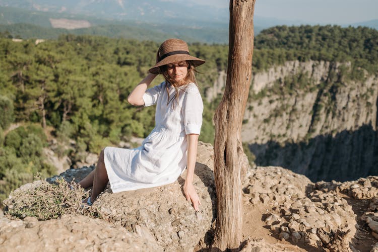 A Woman In White Dress Sitting On The Edge Of A Mountain