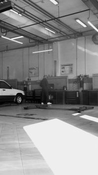 A mechanic performs maintenance in a sunlit car workshop, surrounded by tools and vehicles.