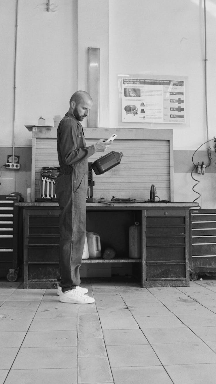 A Man In Coveralls Holding A Smartphone And An Object