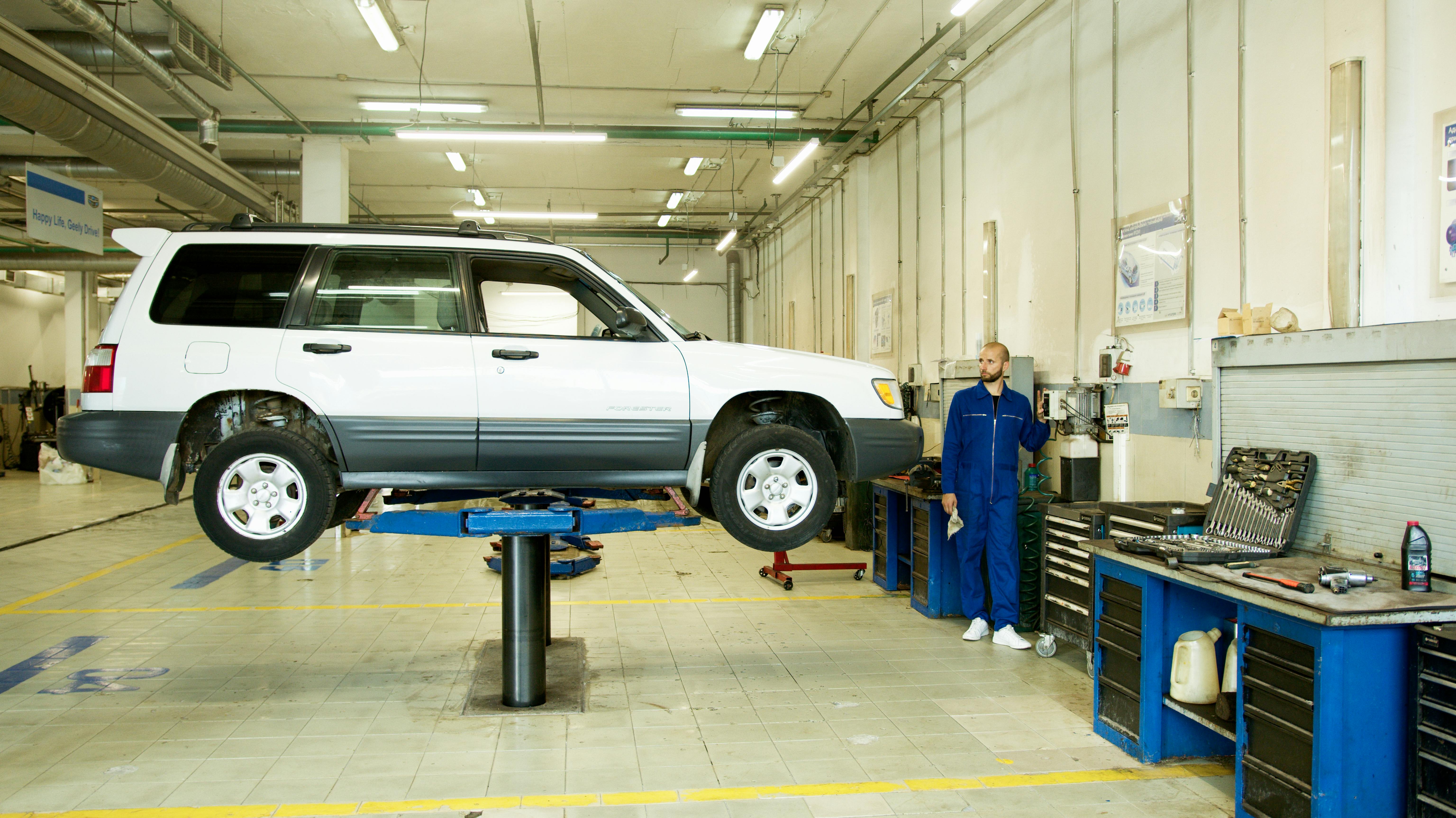 A Man in Blue Coverall Standing Near a White Car by Artem Podrez