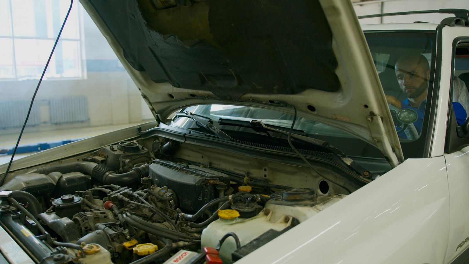 Mécanicien vérifiant le moteur d'un véhicule capot ouvert dans un garage