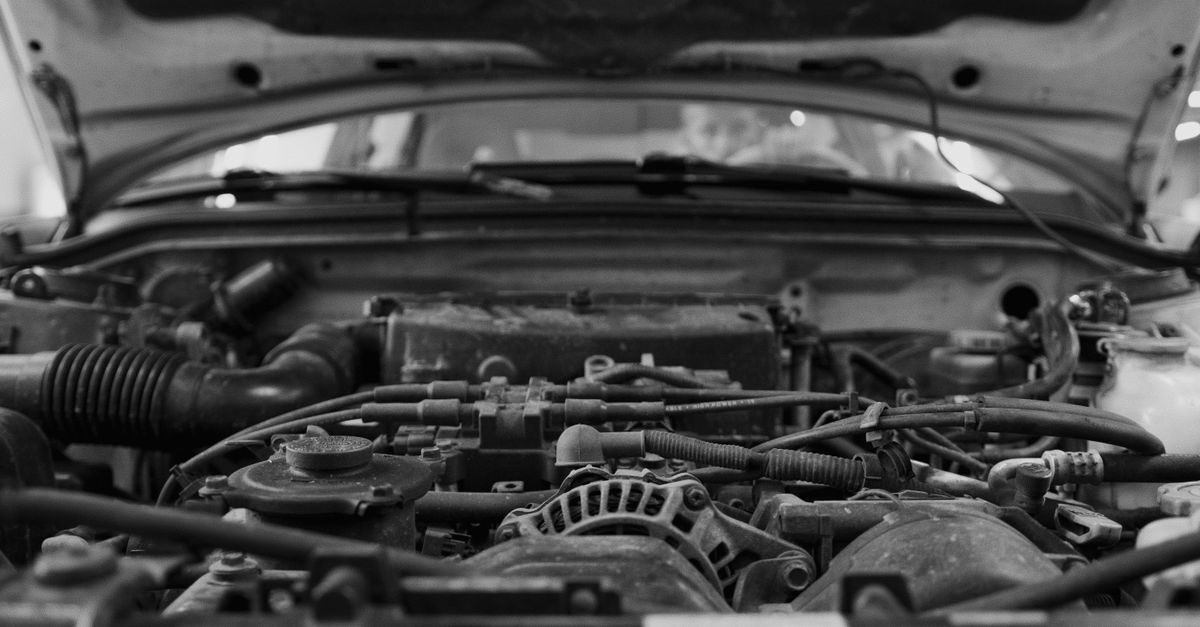 Detailed black and white close-up of a car engine bay with visible components.