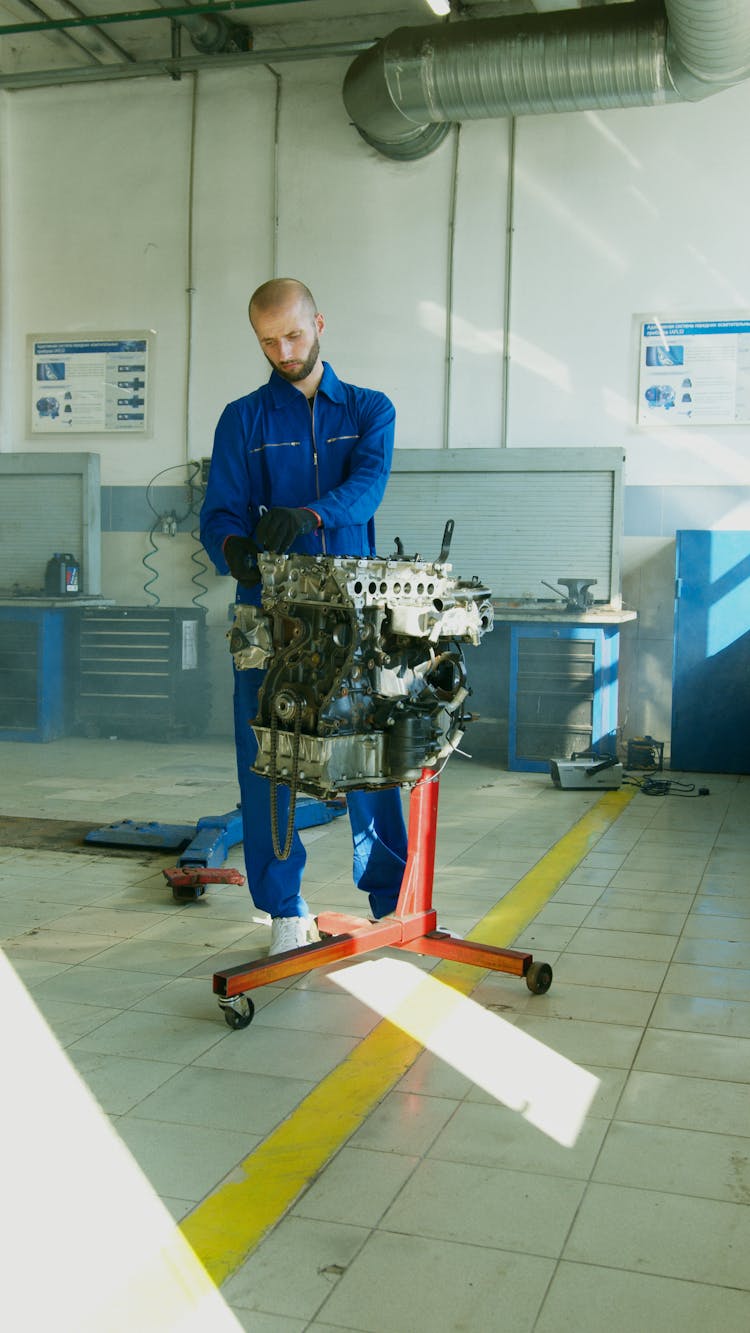 Man In Blue Overalls Checking An Engine